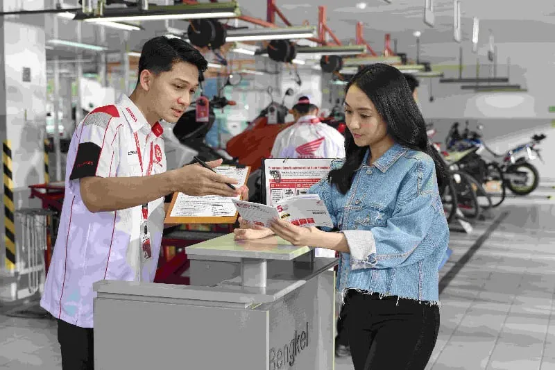Pemilik sepeda motor Honda membaca Buku Pedoman Pemilik & Garansi Sepeda Motor saat melakukan servis di bengkel AHASS.
